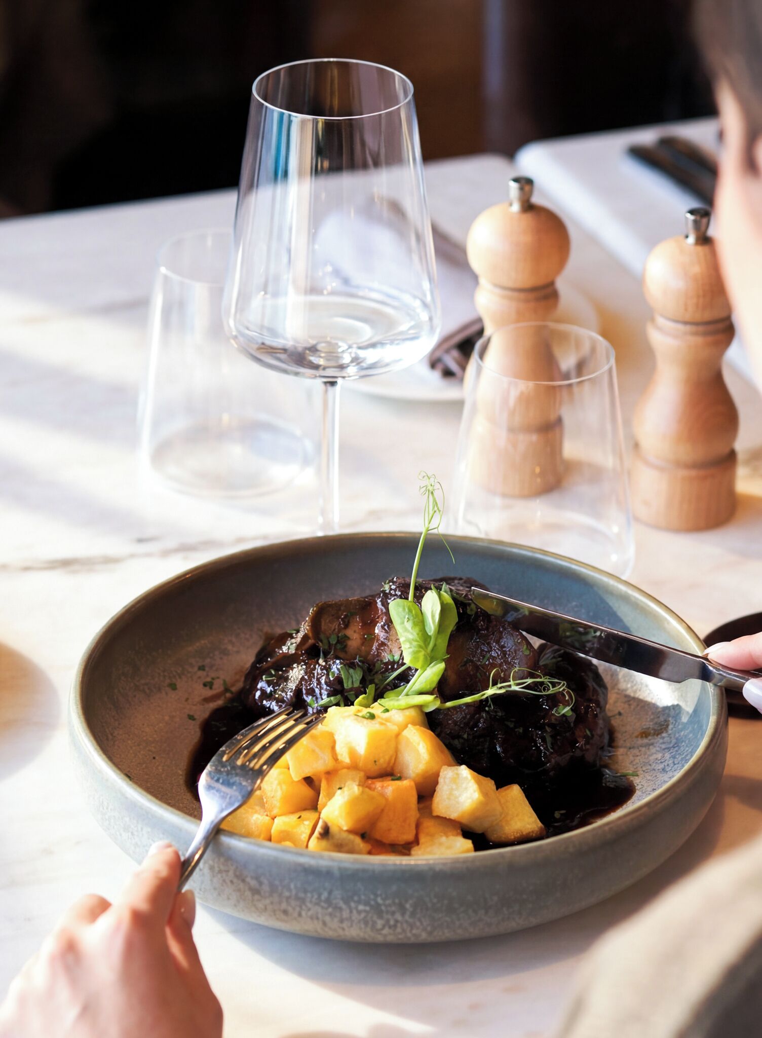Una mesa de comedor con un plato de comida, una copa de vino y un salero y pimentero.