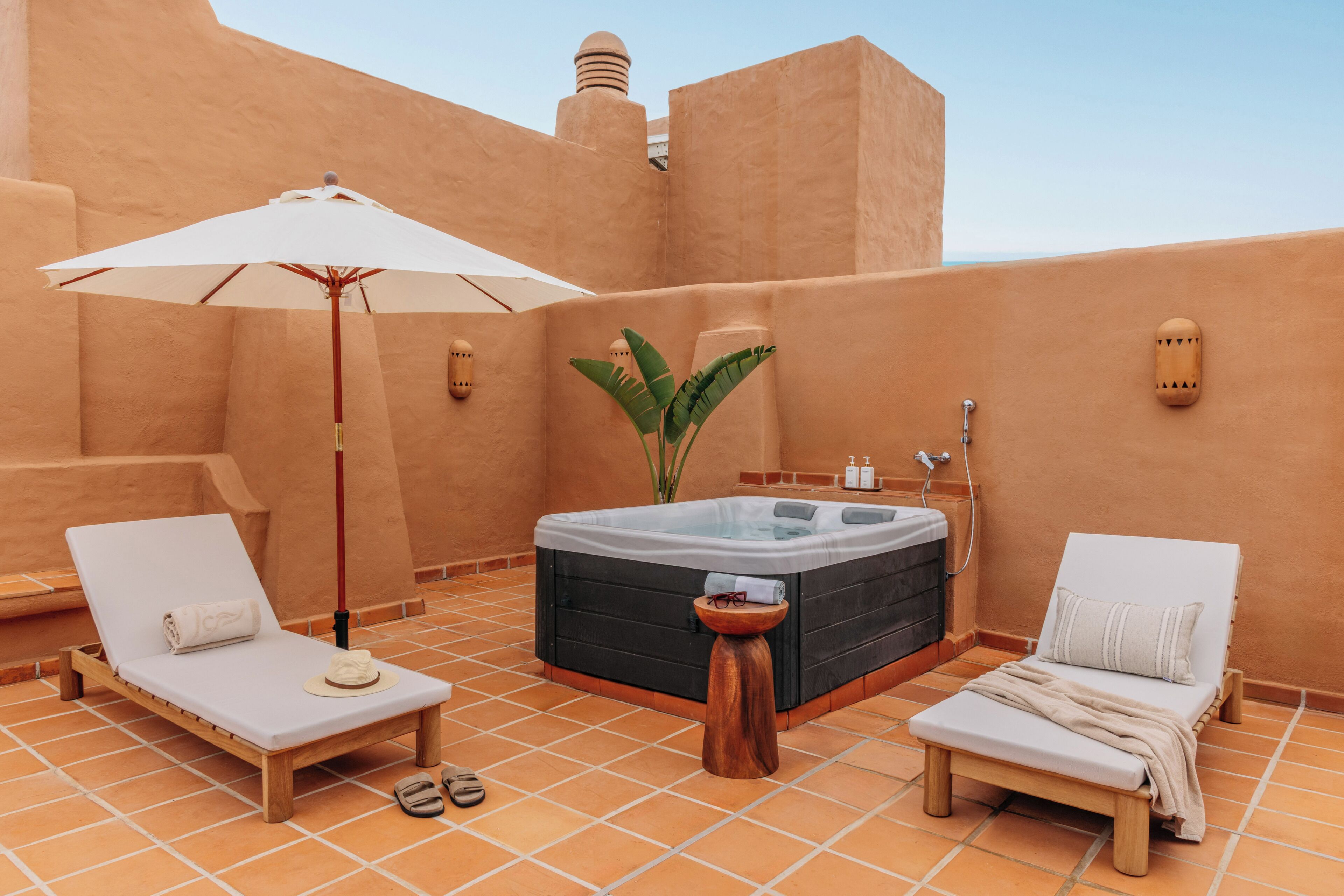 A rooftop terrace with a hot tub, two lounge chairs, an umbrella, and a small table.