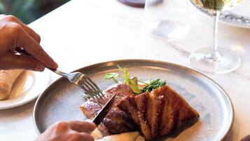 Una persona cenando en una mesa con un plato de comida, una copa de vino blanco y un tenedor.