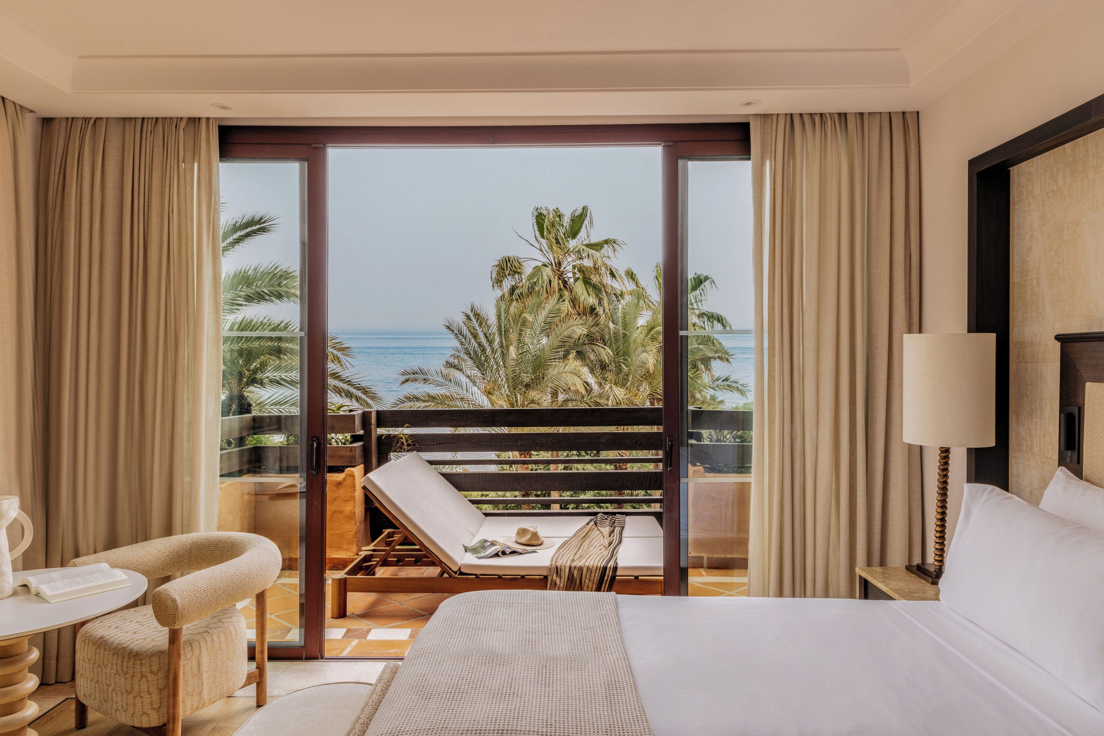 Habitación de hotel con cama, una silla, una mesa y vista al océano.