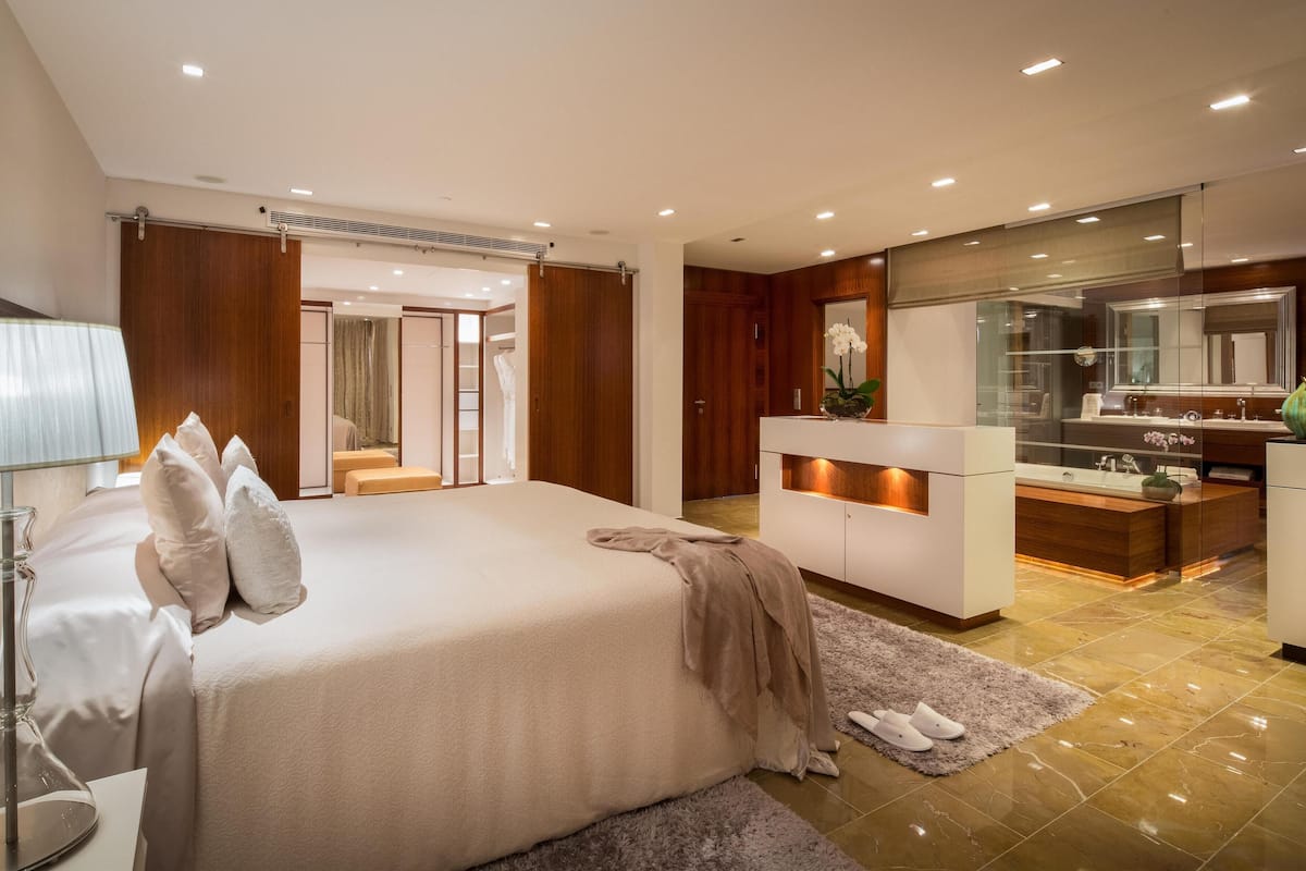 A modern bedroom with a large bed, a vanity with a mirror, and a walk-in closet.