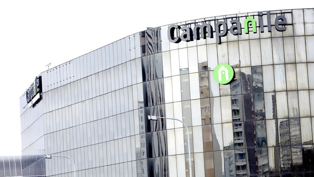 Un bâtiment moderne doté d’une façade en verre réfléchissant, sur laquelle on peut voir l’enseigne « Camparile » et une flèche verte indiquant la direction.