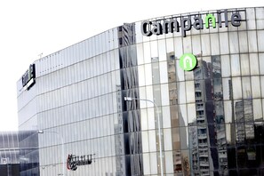 Un bâtiment moderne doté d’une façade en verre réfléchissant, sur laquelle on peut voir l’enseigne « Camparile » et une flèche verte indiquant la direction.