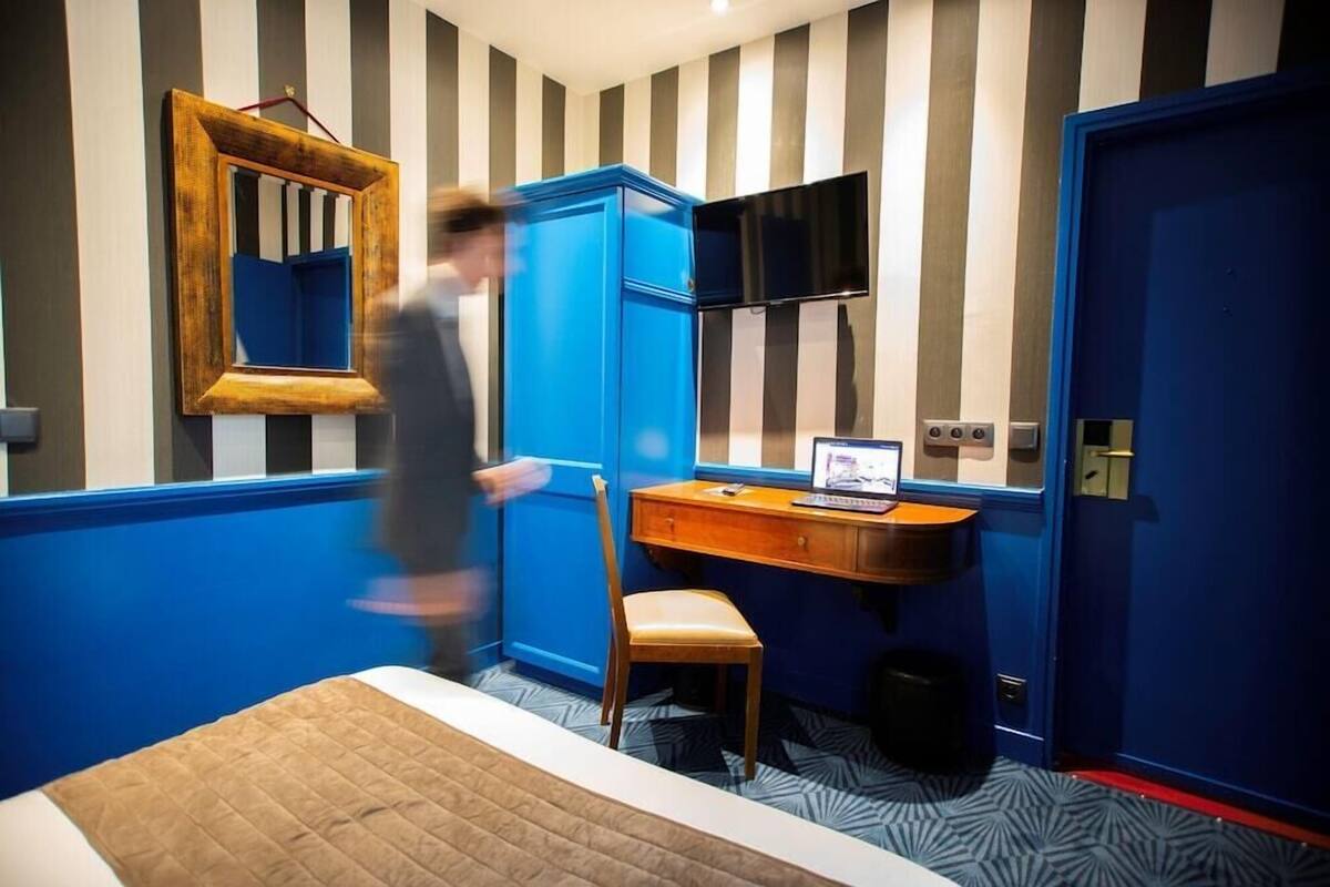 Une chambre d’hôtel avec un lit, un bureau avec un ordinateur, une chaise, une télévision et une armoire bleue.