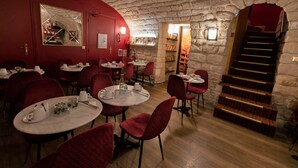 A cozy restaurant with stone walls, red chairs, and round tables.