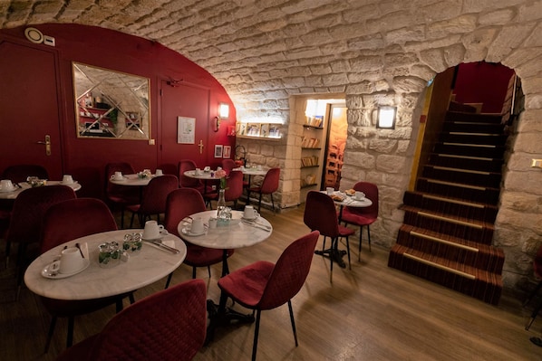 A cozy restaurant with stone walls, red chairs, and round tables. - Hotel du Théâtre by Patrick Hayat (Paris)