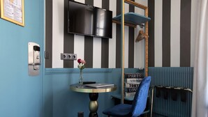 A hotel room with a striped wall, a flat-screen TV mounted above a table with a laptop and a vase of flowers.