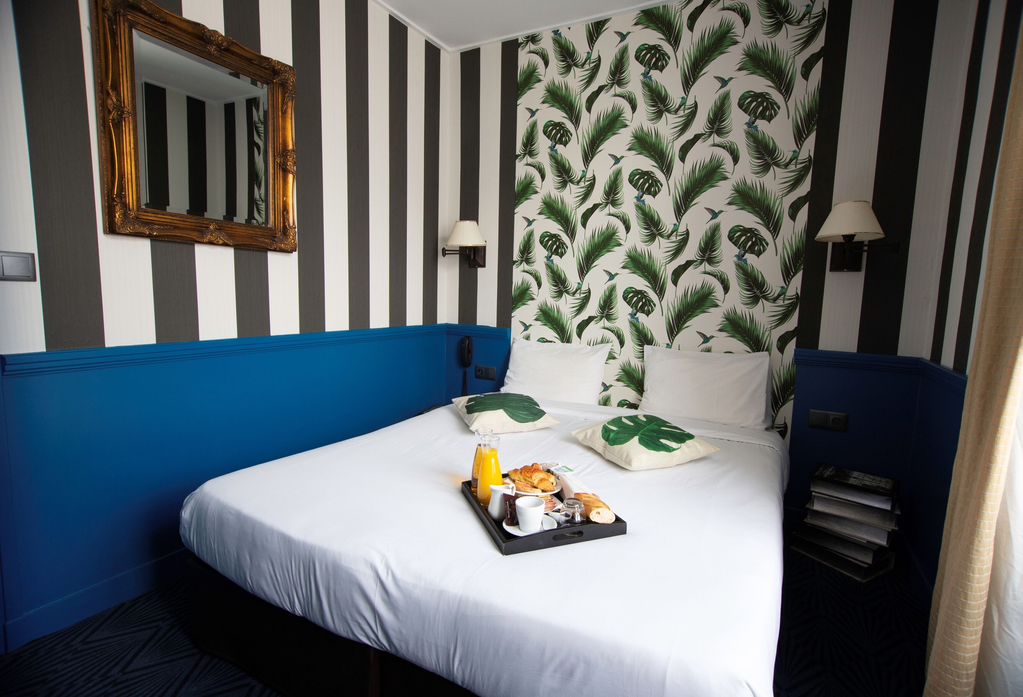 A hotel room with a bed, a tray of breakfast items, a mirror, striped wallpaper, and a blue accent wall.