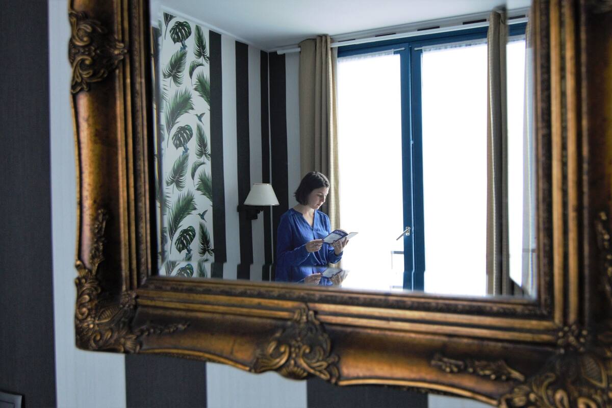 Une pièce avec un grand miroir, une fenêtre avec des rideaux et une lampe fixée au mur.