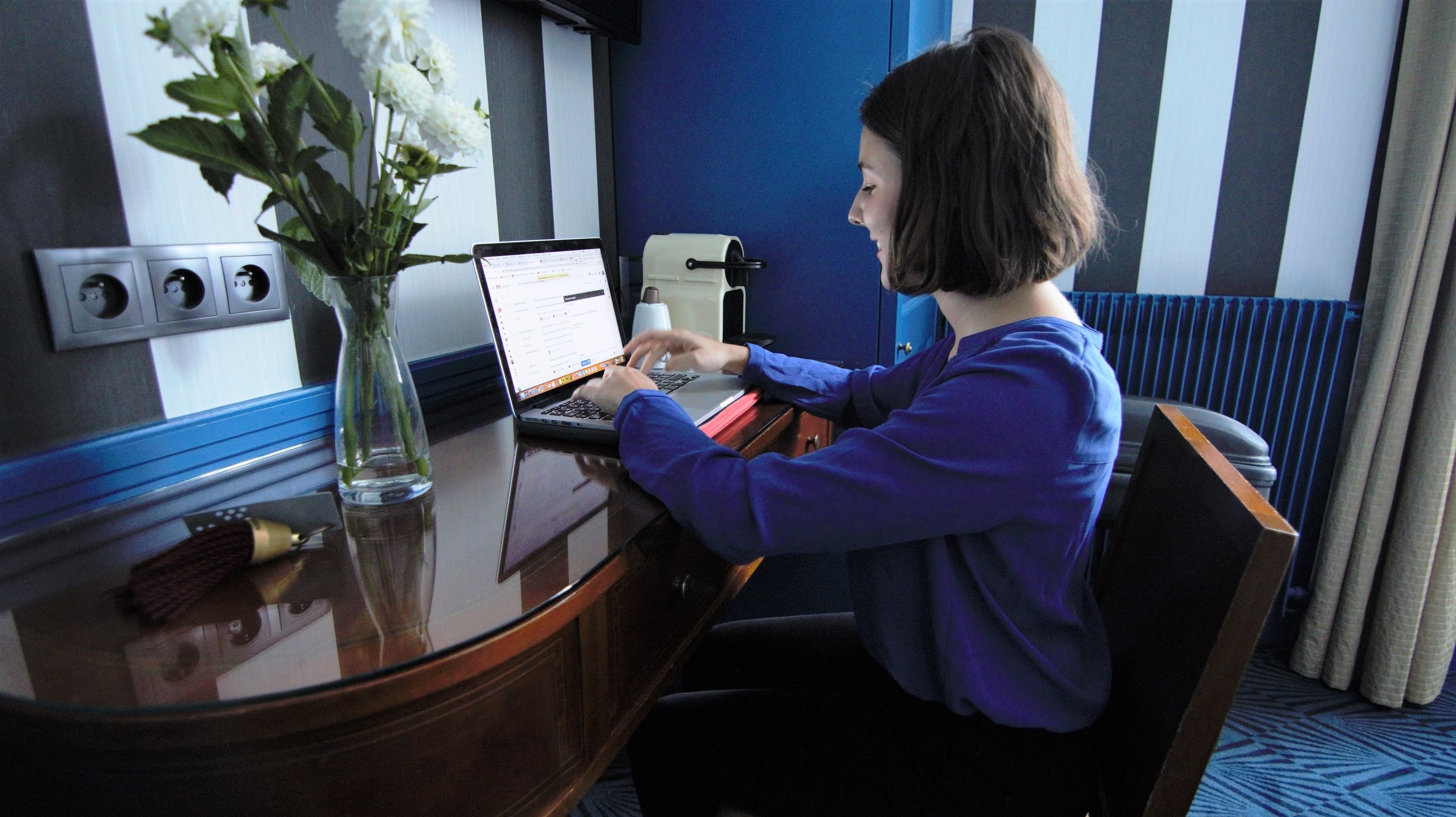 A person working at a desk with a laptop, a vase with flowers, and a radiator in the background.