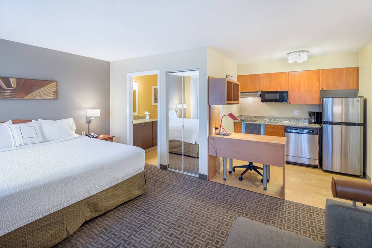 Habitación de hotel con cama, escritorio, kitchenette y baño.