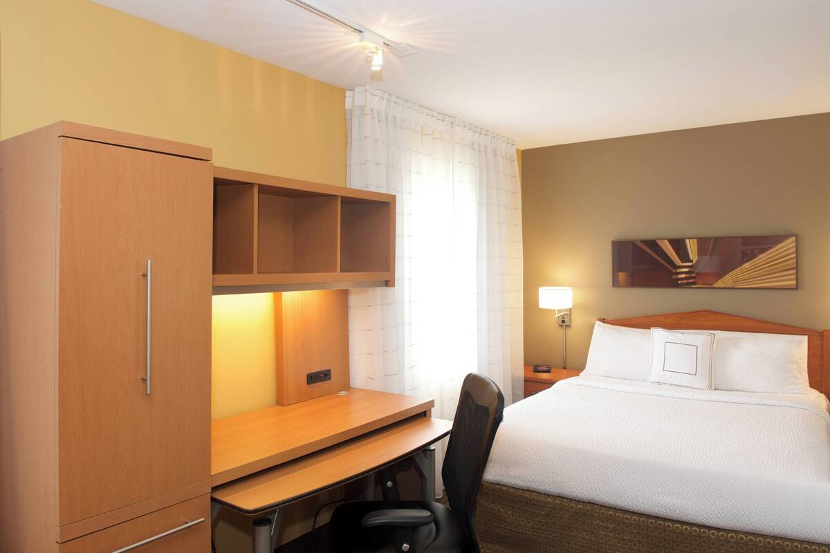 Una habitación de hotel con cama, escritorio, silla y armario.