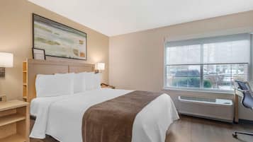 A hotel room with a bed, bedside tables, a window with a view, and a wall-mounted air conditioner.