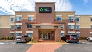 Un hotel Stay America con fachada de ladrillo, entrada al vestíbulo y zona de estacionamiento.