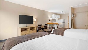 Habitación de hotel con dos camas, un escritorio con silla, televisión, kitchenette y un secador de pelo en la pared.