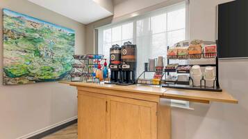 A kitchen counter with coffee makers, a beverage dispenser, and a coffee station with disposable cups and a menu.