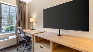 Habitación de hotel con un ventanal grande, un escritorio con silla, un televisor de pantalla plana, una lámpara y un calentador.