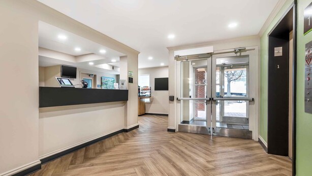 Zona de recepción con mostrador, televisor y puerta de vidrio que da al exterior.