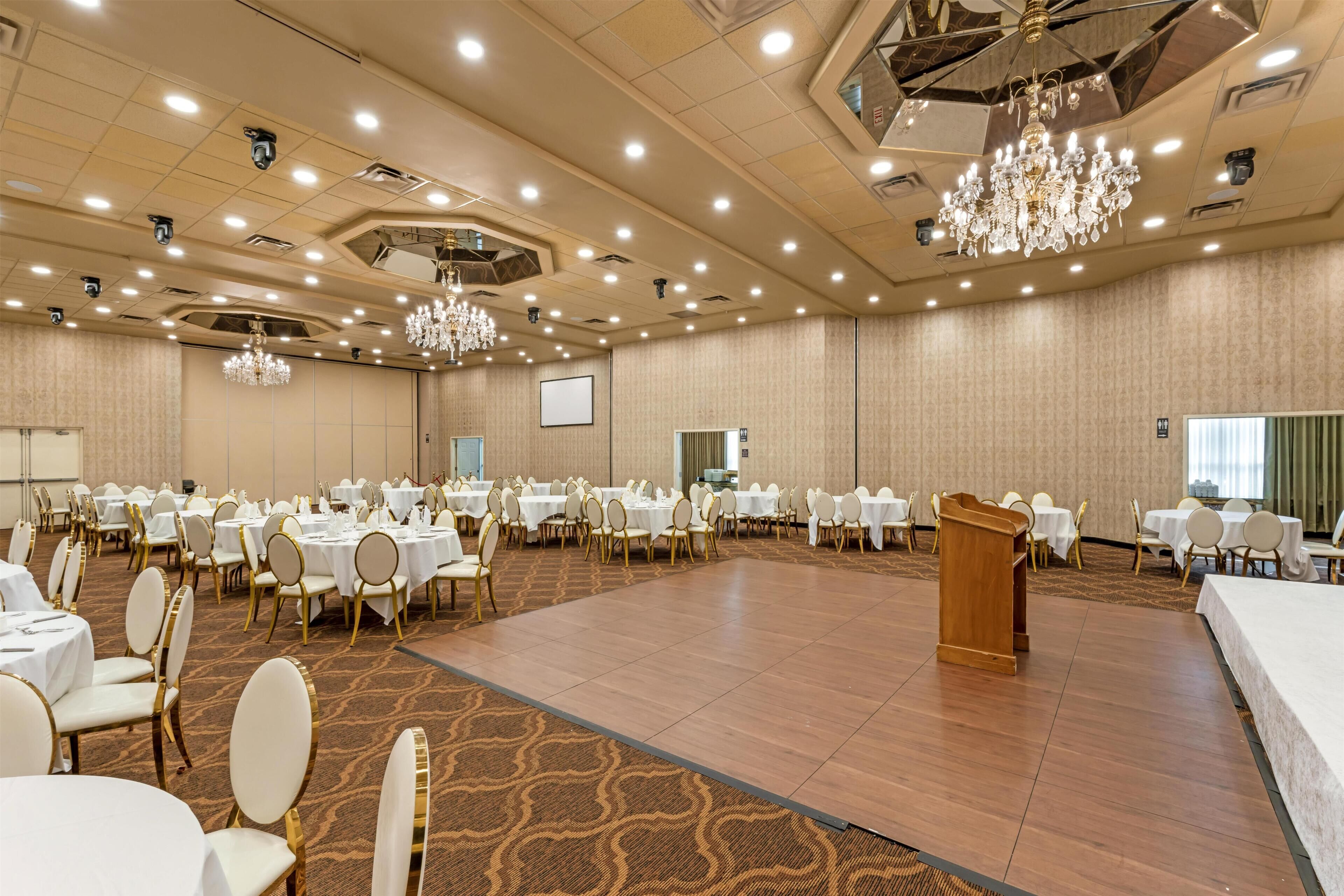 Un amplio salón de conferencias con mesas redondas, sillas, un atril y candelabros.