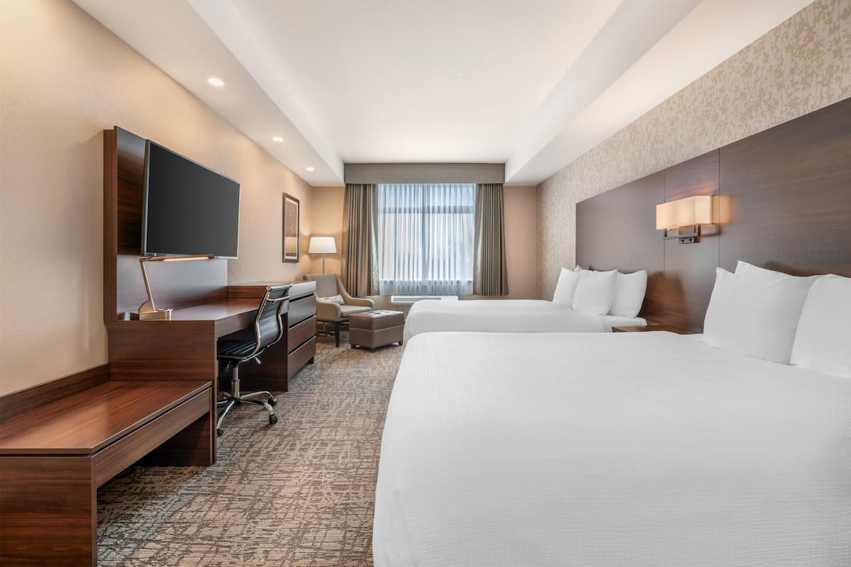 Habitación de hotel con una cama grande, un escritorio con silla, un televisor y una ventana con cortinas.