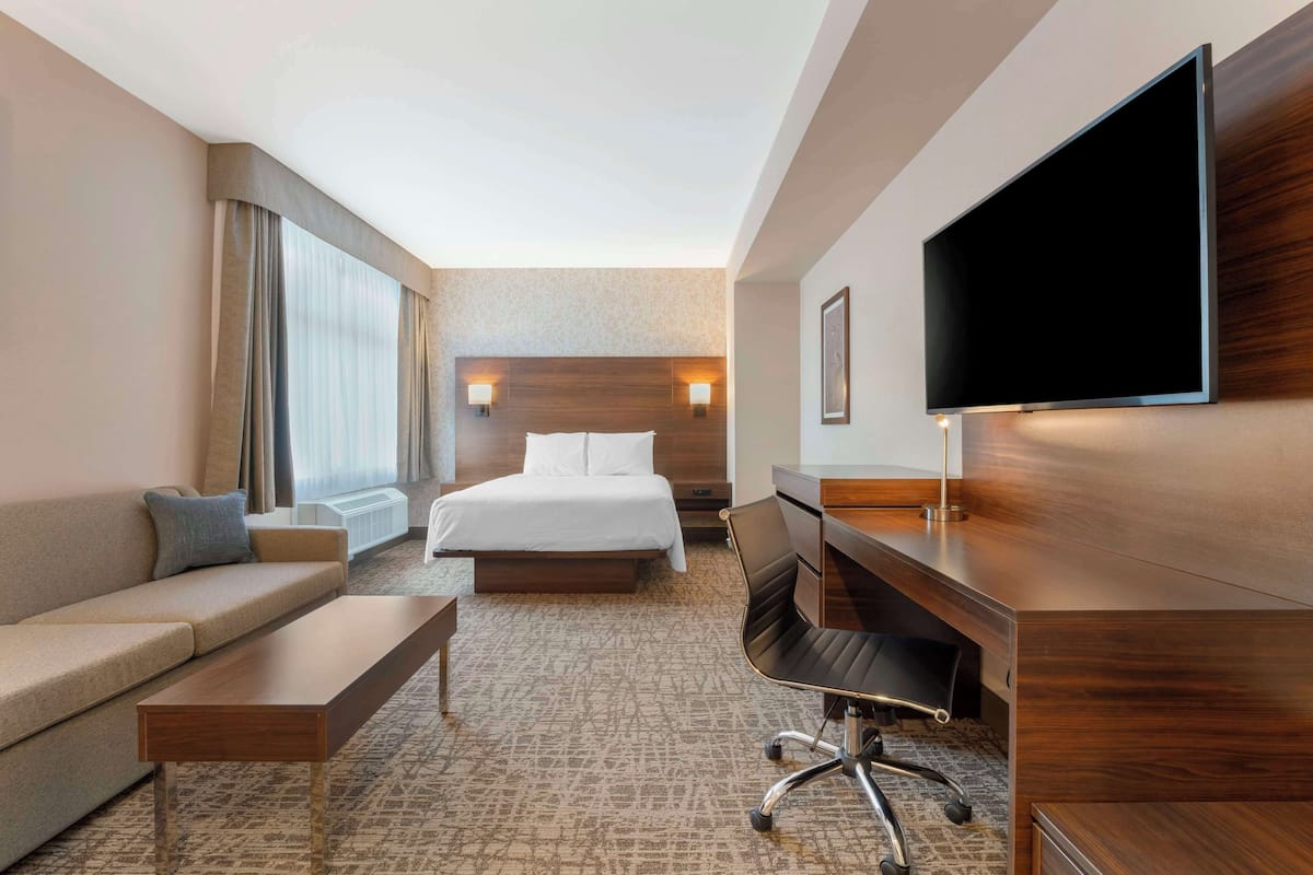 Habitación de hotel con cama, sofá, escritorio, silla, televisor y un ventanal grande.