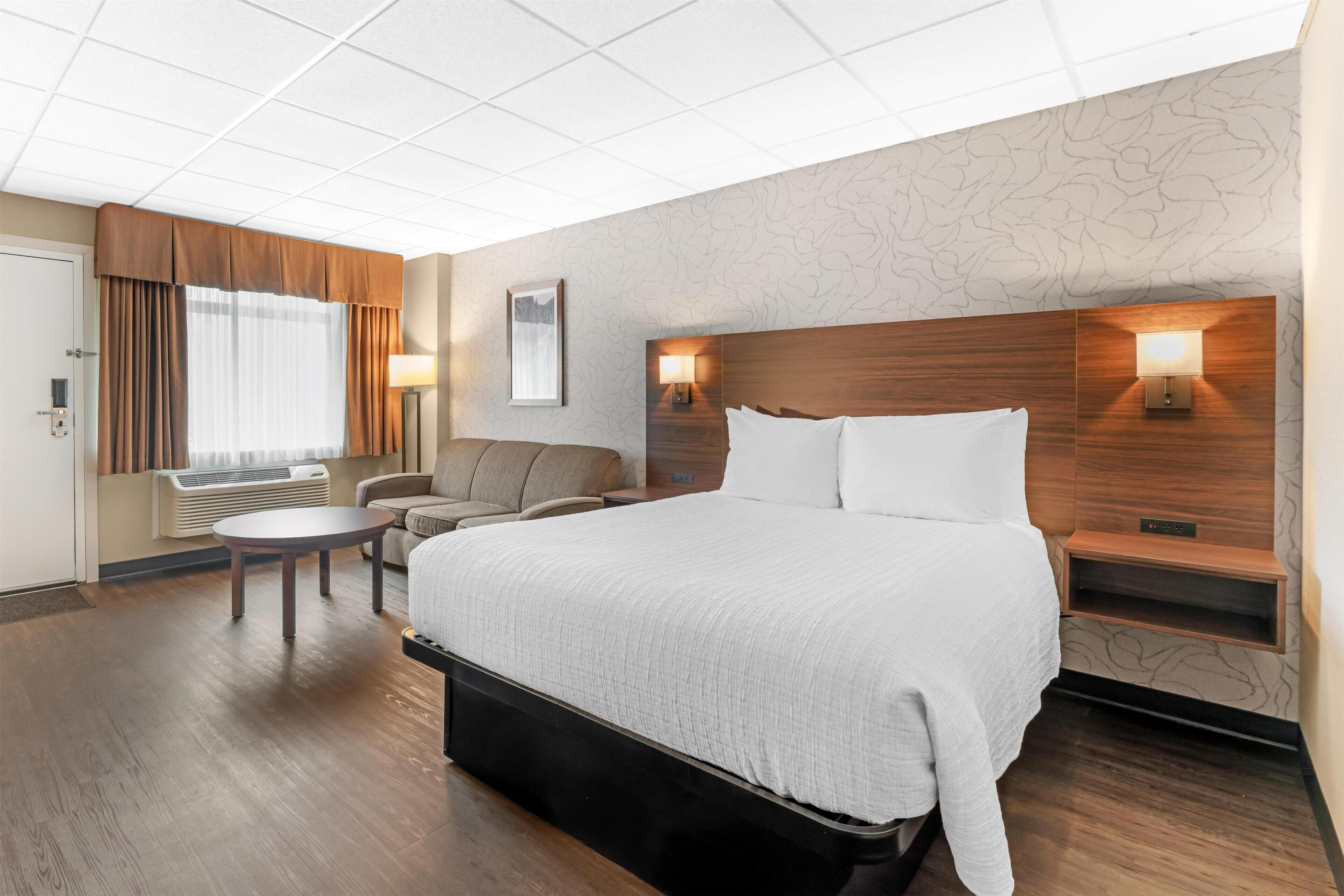 A hotel room with a large bed, a round table, a sofa, and a wall-mounted lamp.
