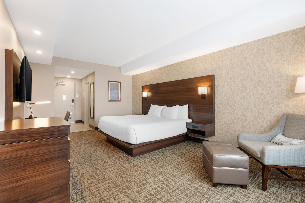 Habitación de hotel con cama, escritorio, silla, televisor y lámpara de pared.
