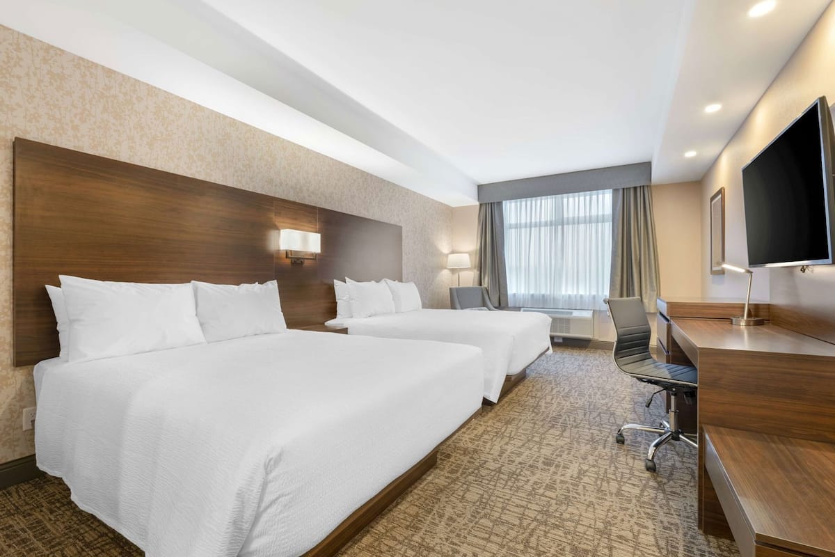 Habitación de hotel con dos camas, un escritorio, una silla, un televisor y una ventana con cortinas.