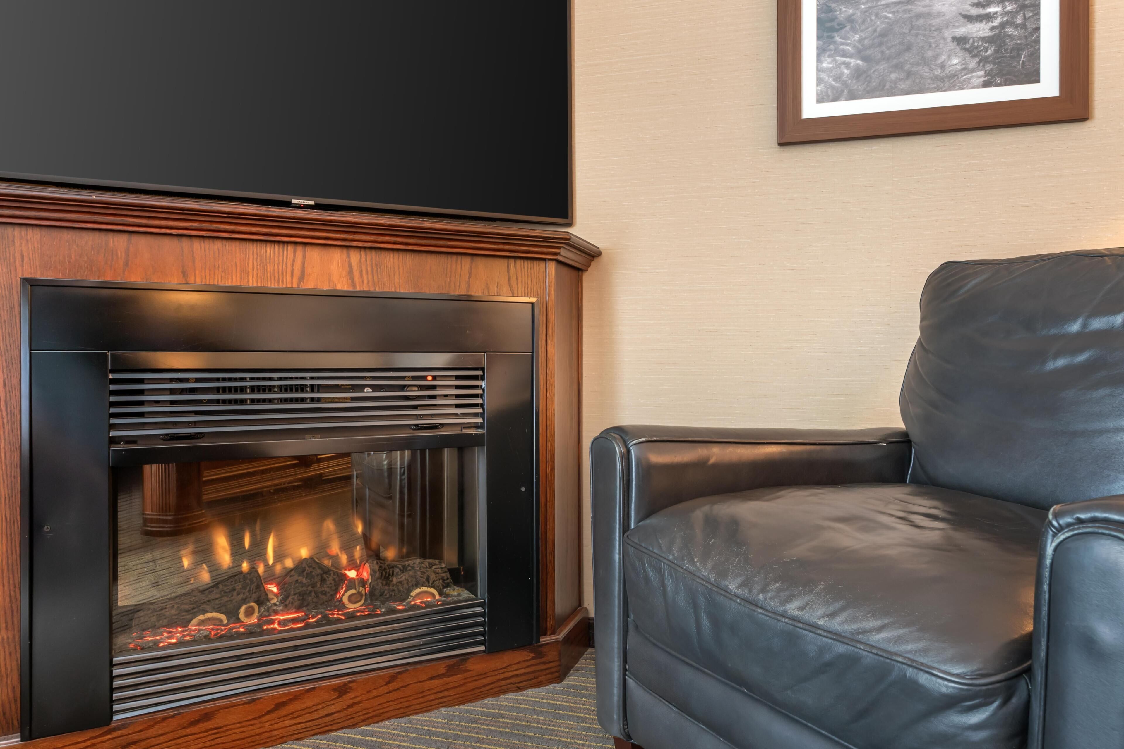 Una chimenea de diseño moderno, un sillón de cuero negro y un cuadro en la pared.