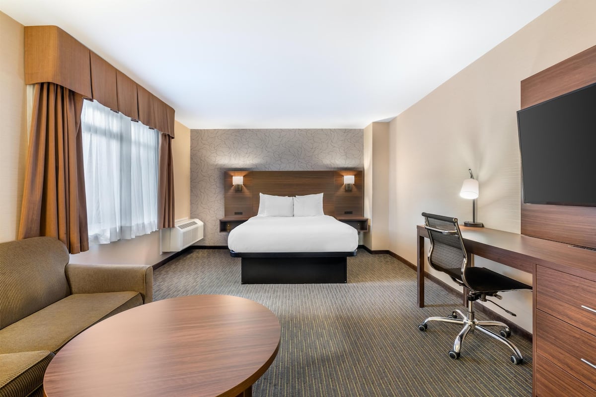 Una habitación de hotel con cama, escritorio, silla, sofá y televisor.