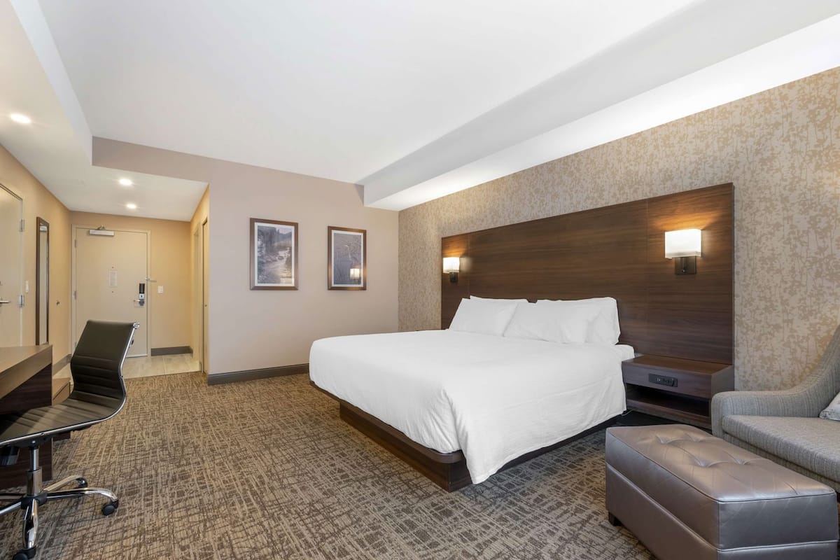 Una habitación de hotel con una cama grande, un escritorio, una silla y un pequeño reposapiés.