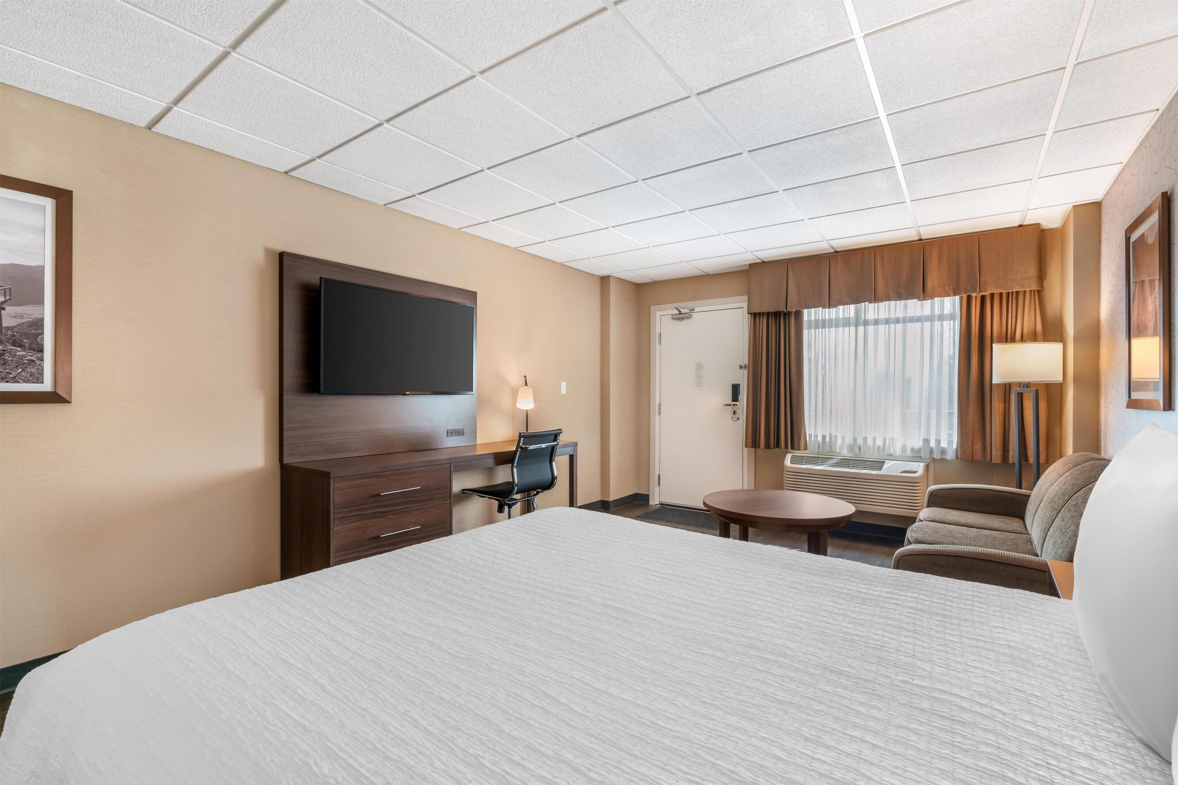 Habitación de hotel con una cama grande, un escritorio con una silla, un televisor, una ventana con cortinas y un equipo de aire acondicionado.
