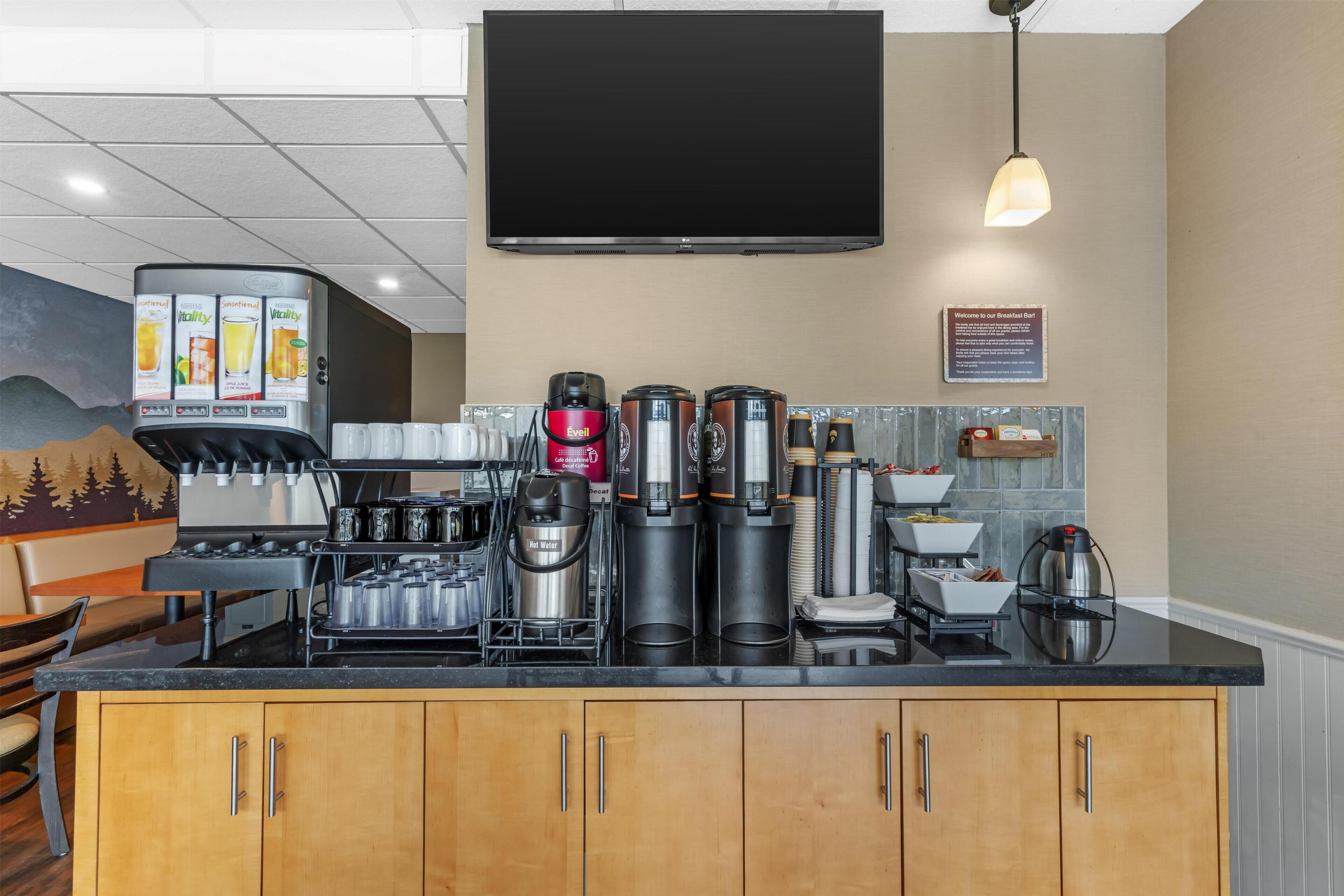 A modern kitchen with a coffee station, a flat-screen TV, and a breakfast sign.