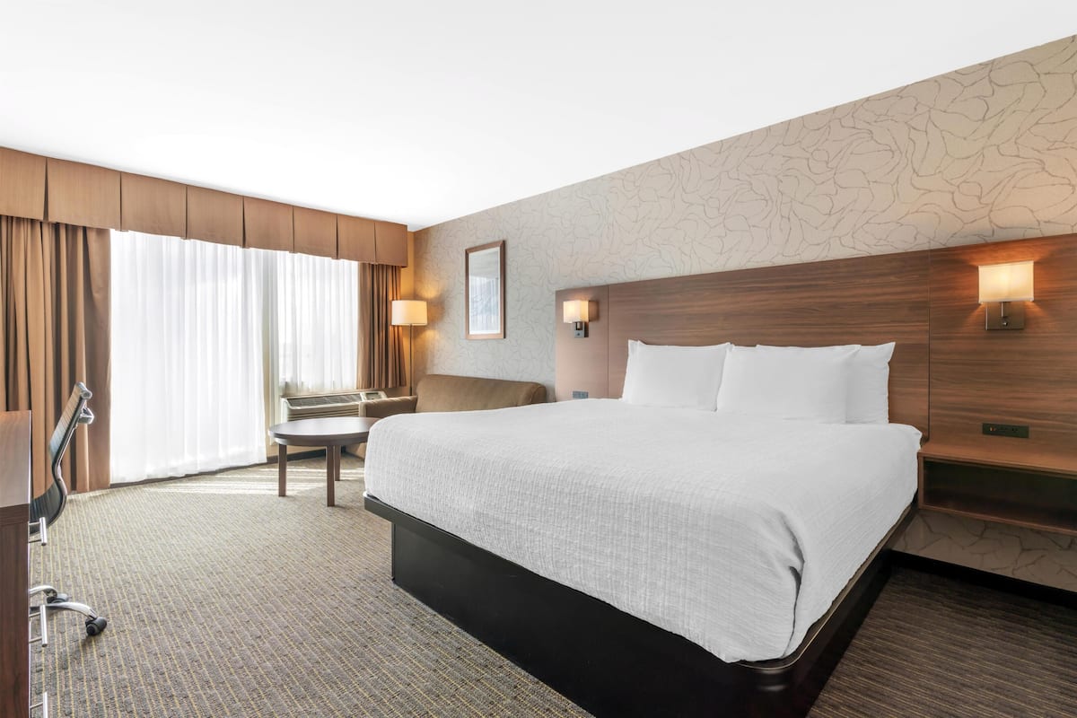 Una habitación de hotel con una cama grande, un escritorio, una silla y una ventana con cortinas.