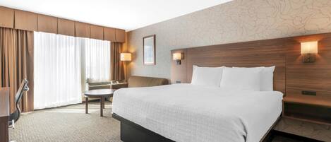 A hotel room with a large bed, a desk, a chair, and a window with curtains.