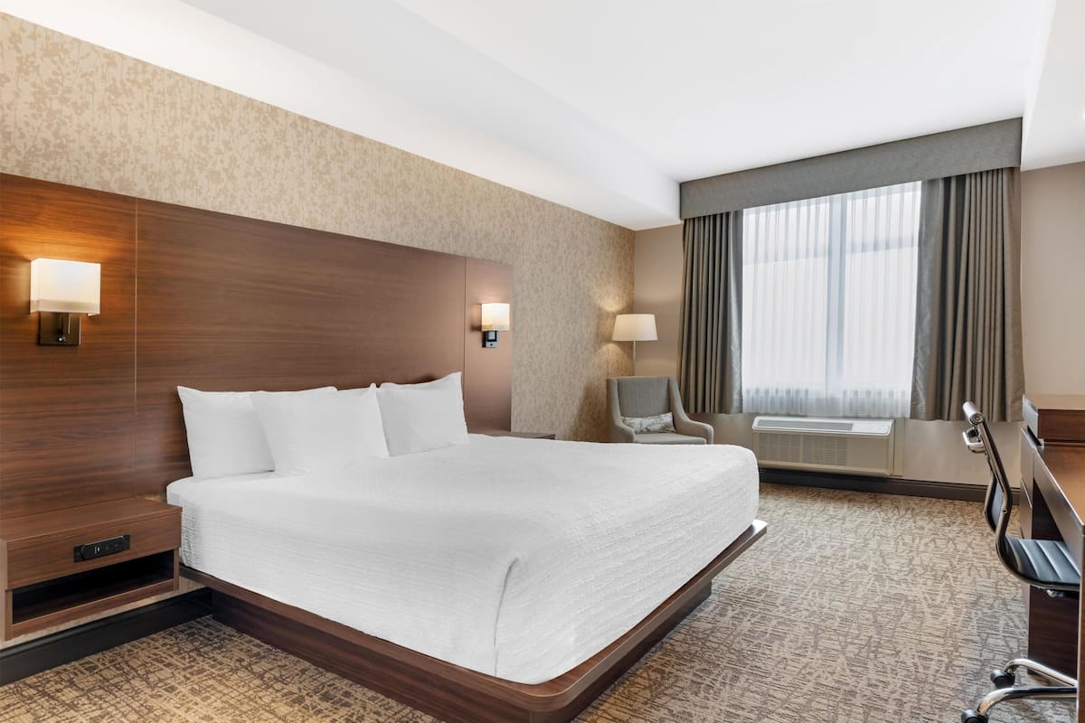 Una habitación de hotel con una cama grande, un escritorio, una silla, una lámpara y una ventana con cortinas.