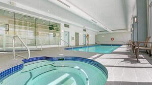 Una amplia piscina interior con agua cristalina, rodeada por un suelo de baldosas y equipada con un pasamanos metálico.