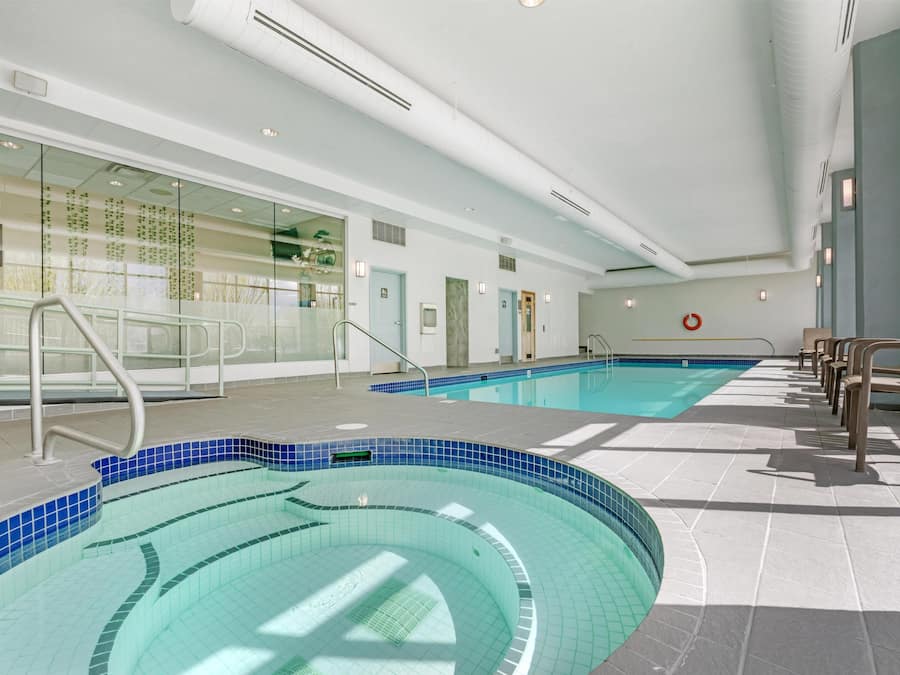 Una amplia piscina interior con agua cristalina, rodeada por un suelo de baldosas y equipada con un pasamanos metálico.