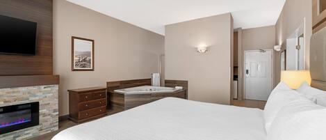 A hotel room with a large bed, a fireplace, a television, a bathroom with a bathtub, and a mirror.