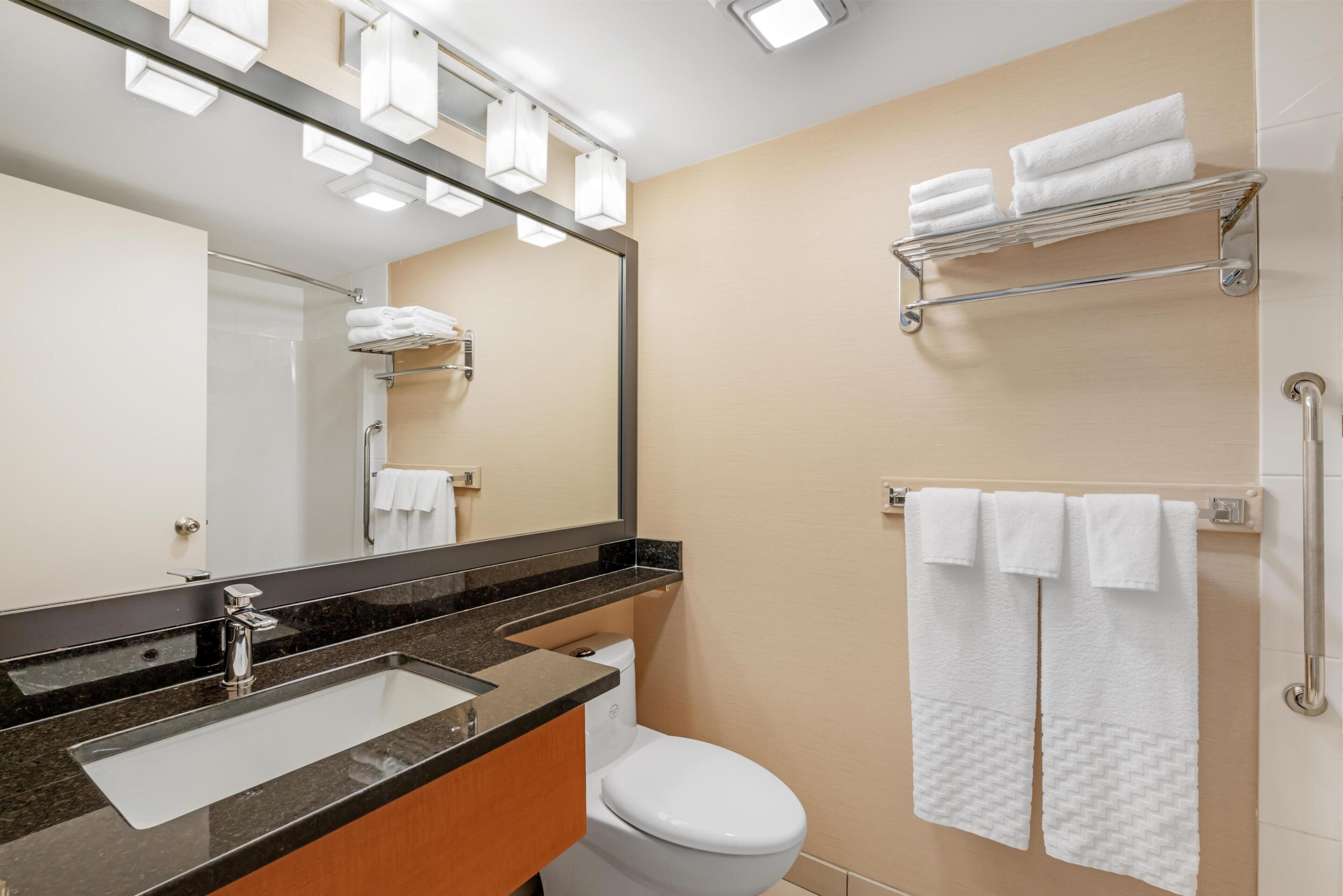 A modern bathroom with a sink, mirror, toilet, towel rack, and shower area.
