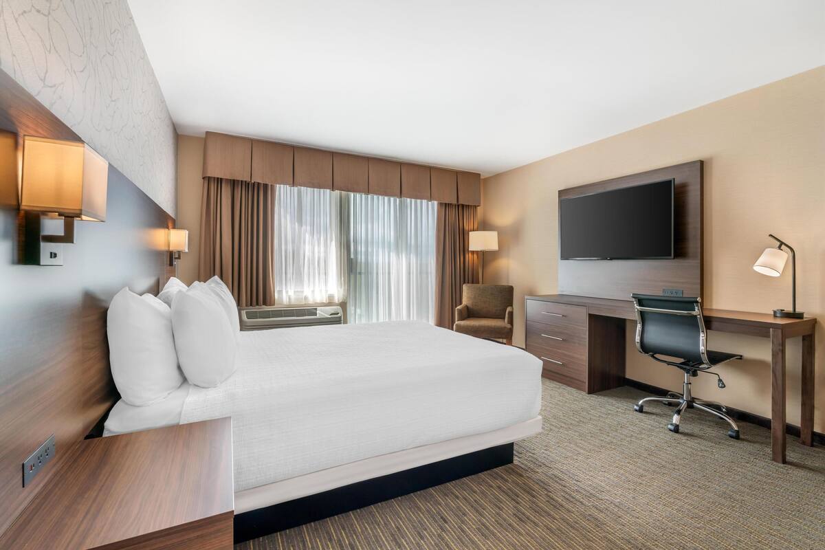 Habitación de hotel con cama, escritorio, silla, televisor y dos lámparas de pared.