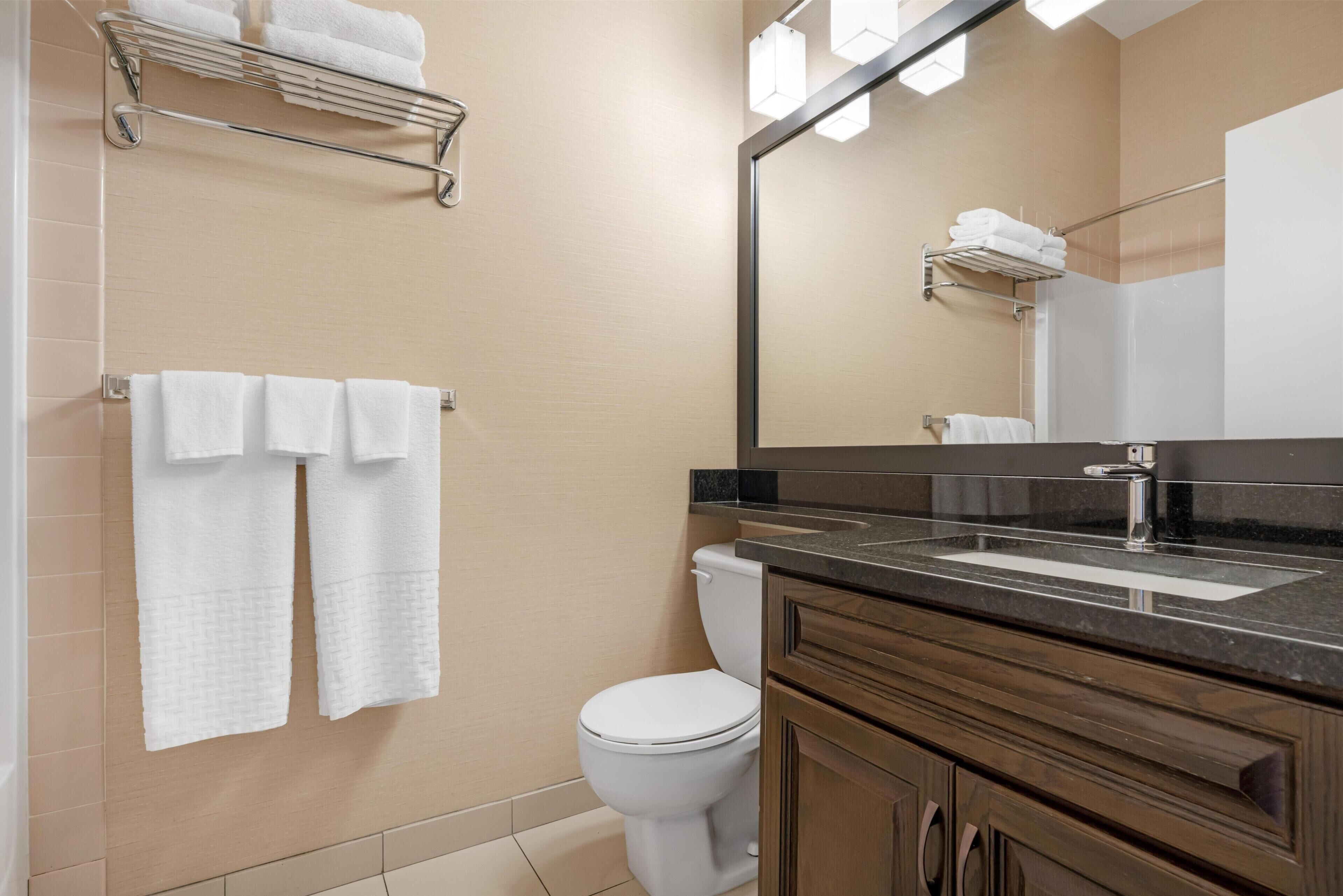 A bathroom with a toilet, a sink, a mirror, and towels on a rack.