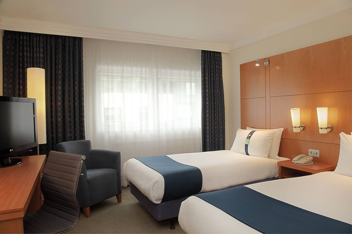 A hotel room with two beds, a desk with a TV, a chair, and a bedside table with a phone.