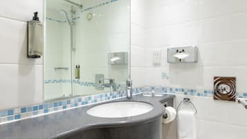 A modern bathroom with a granite countertop sink, a large mirror, a toilet, and a trash can.