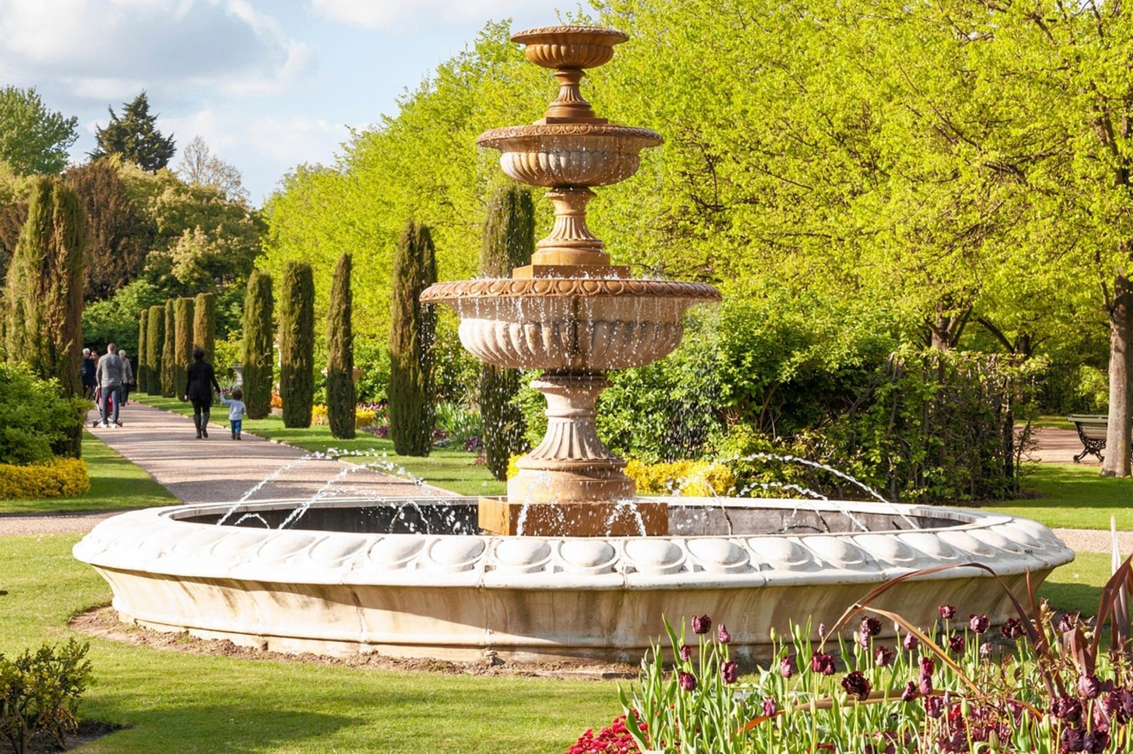 A multi-tiered fountain in a park with manicured hedges and tulips.
