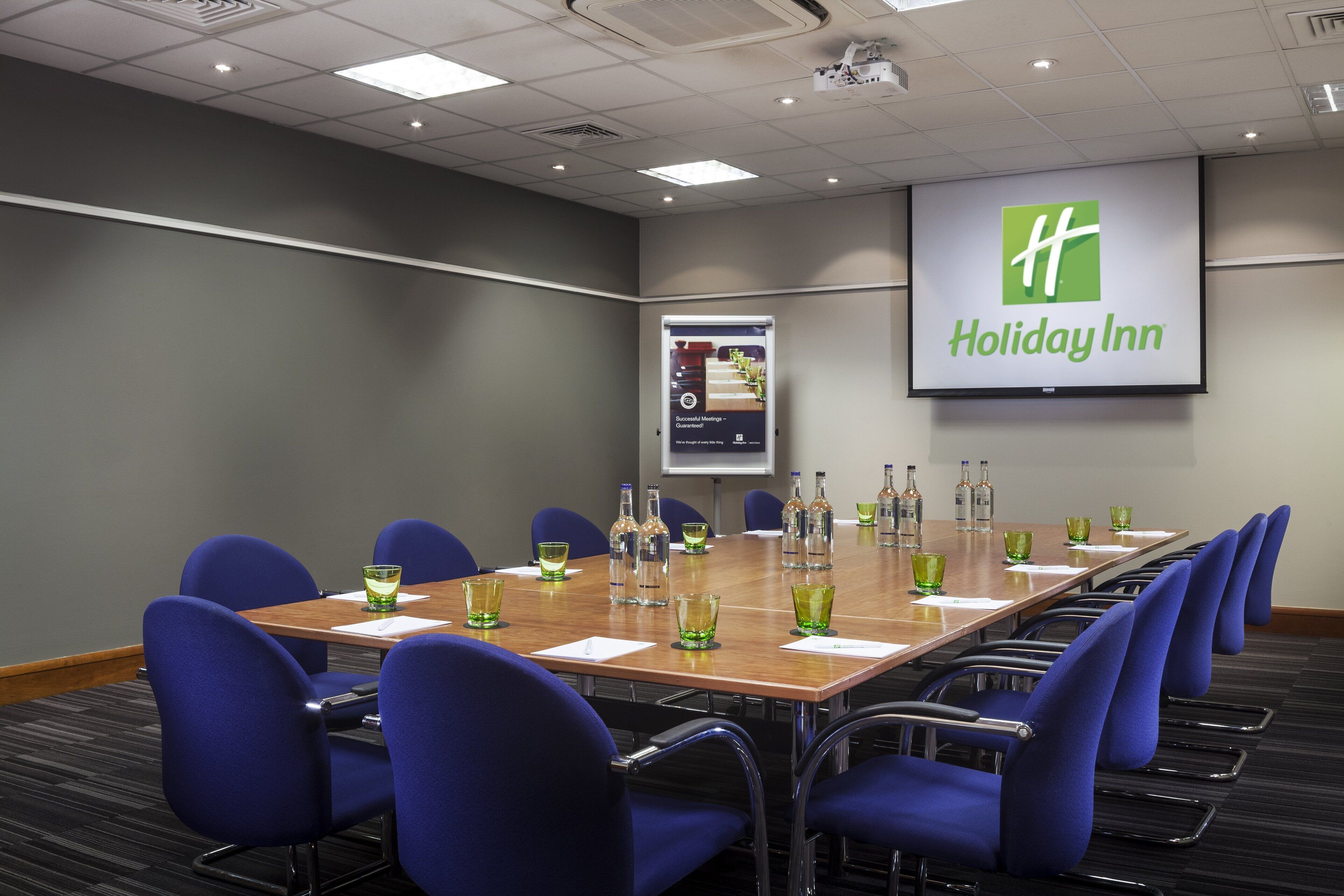 A conference room with a long table, blue chairs, and a Holiday Inn sign on the wall.