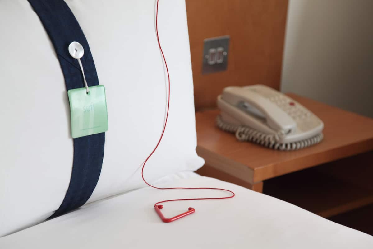 A white pillow with a green tag, a red cord, and a white telephone on a wooden surface.