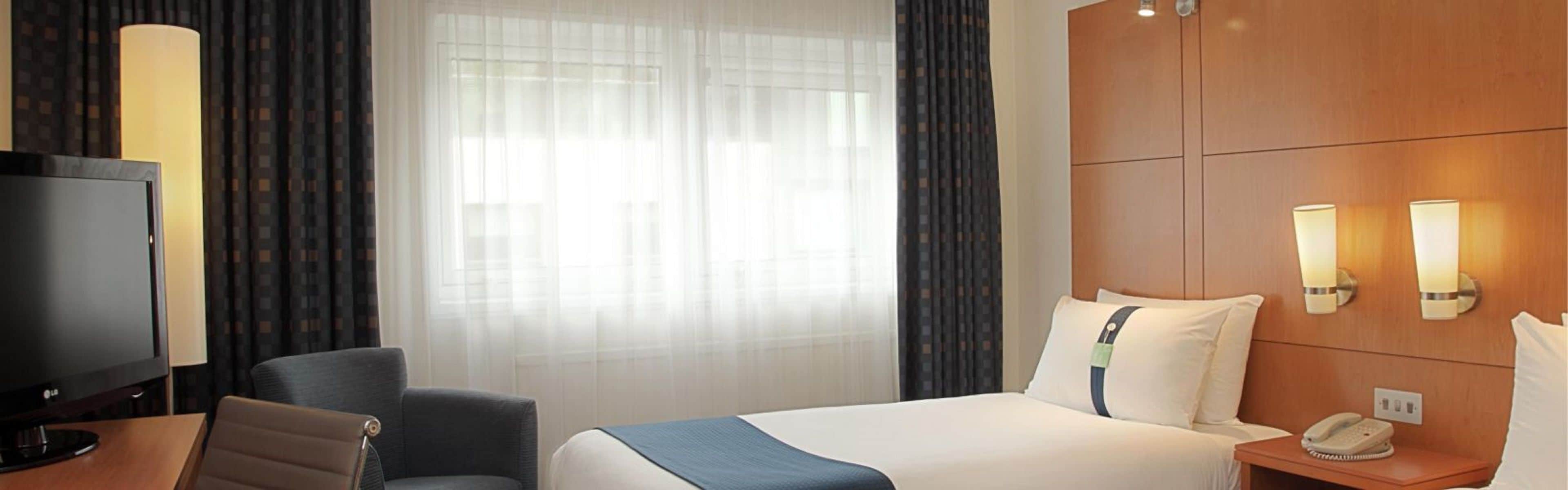 Une chambre d’hôtel équipée d’un lit, d’une télévision, d’une chaise, d’un bureau, d’une lampe et d’un téléphone.