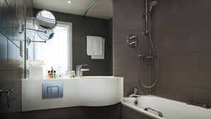 Une salle de bain moderne avec un meuble-lavabo aux lignes courbes, un grand miroir, une douche équipée d’un pommeau de douche à main et une baignoire blanche.