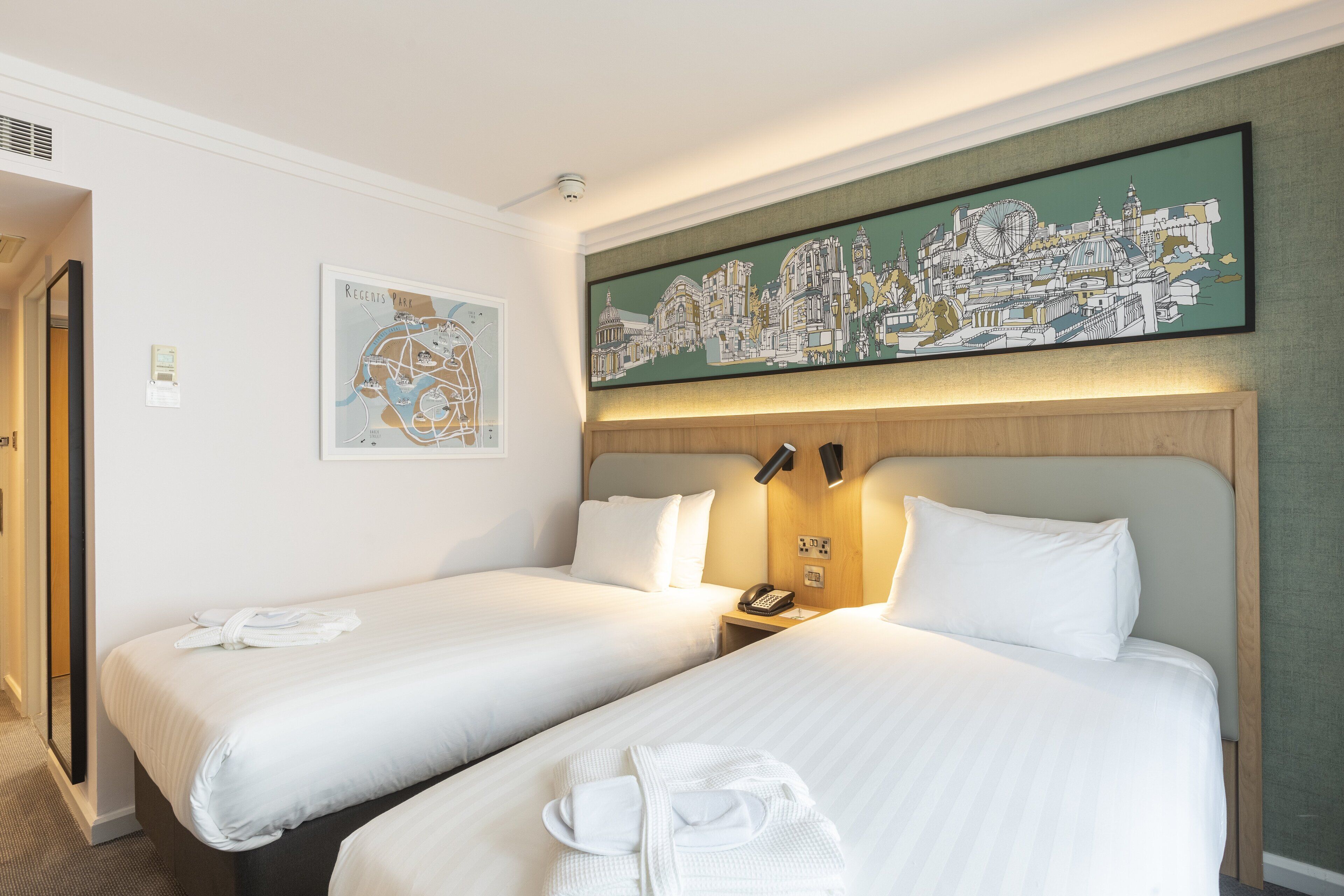 A hotel room with two beds, a cityscape artwork, a map, and a phone on the nightstand.